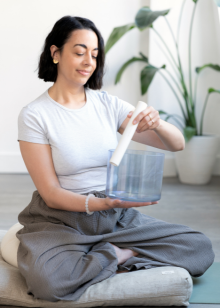 Woman sitting on a yoga mat holding a clear container with a white object inside.