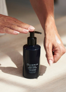 Black bottle of Oliverum hand lotion being held by a person on a light background
