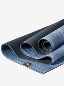 Rolled premium yoga mat in gradient blue colors with Manduka brand logo, non-slip texture, close-up side shot, professional exercise equipment, durable workout mat.