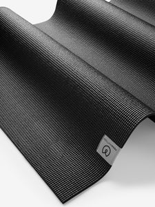 Black textured yoga mat from Lululemon with visible brand logo, non-slip surface detail, shot from an angled side perspective