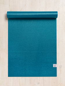 Teal textured yoga mat partially rolled up, top view on a wooden floor, eco-friendly high-grip exercise mat with visible brand logo