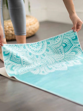 Turquoise patterned yoga mat with intricate mandala design, side shot of rolling out non-slip exercise mat on wooden floor, fitness accessory for yoga and meditation practice.