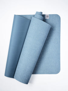 Blue textured yoga mat partially rolled next to fully unrolled mat, top view, with visible logo on corner.