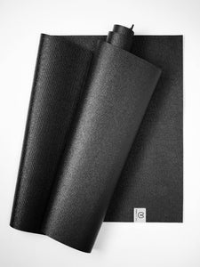 Black textured yoga mat rolled up beside an unrolled one, overhead view, exercise equipment, fitness accessory, non-slip surface design.