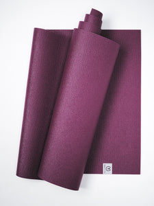 Purple textured yoga mat partially rolled with visible logo tag isolated on white background, top view.