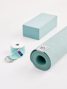Aqua blue yoga mat with yoga block and carrying strap, eco-friendly material, textured non-slip surface, front view on white background.