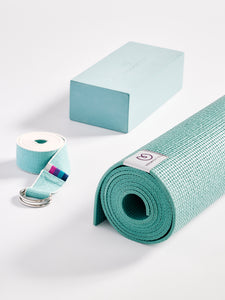 Teal yoga mat rolled up beside a yoga block and strap, textured non-slip surface, yoga accessories photographed on a white background, eco-friendly yoga equipment, wellness and fitness products.