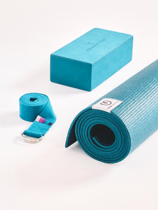 Teal yoga mat rolled up, with a matching yoga block and strap, side view on a white background, textured non-slip surface, yoga accessories, studio equipment