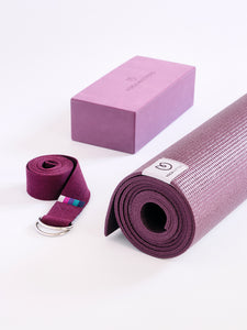 Purple yoga mat rolled up with matching yoga strap and block from YogaAccessories brand, photographed on a white background, side view.