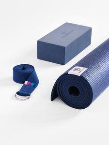 Blue yoga mat rolled up with carrying strap and foam block, side view on white background, textured non-slip surface, YogaFitness brand visible.