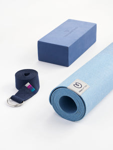 Blue yoga mat partially rolled with textured surface alongside yoga block and strap, front view on white background.
