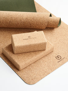 Yogamatters branded cork yoga mat in natural brown with rolled front edge and green underside, alongside matching cork yoga blocks, studio quality, eco-friendly, non-slip textured surface, photographed from side angle.