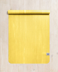 Bright yellow yoga mat on wooden floor, top view, textured non-slip surface, rolled edge, Lululemon brand visible