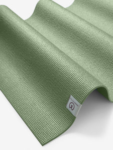Green textured yoga mat from side angle with visible brand logo, non-slip surface design for yoga and fitness enthusiasts.