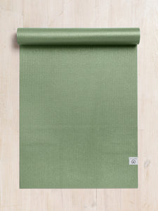 Green textured yoga mat partially rolled up with visible brand logo, shot from above on a light wooden floor, fitness and exercise equipment.