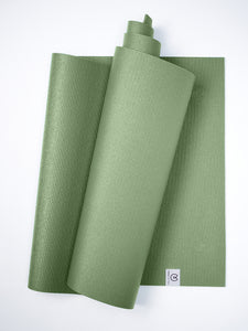 Green textured yoga mat partially rolled with visible brand logo on white background, top view, non-slip surface, exercise equipment, fitness accessory, wellness and yoga practice, durable material.