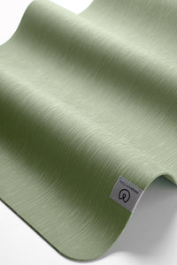 Green textured yoga mat displayed semi-rolled from the side with visible brand label, premium non-slip exercise mat for fitness and wellness.