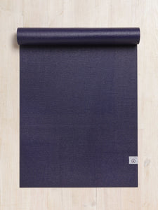 Purple yoga mat partially rolled up on a wooden floor shot from above showing textured surface and branded corner