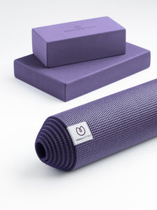Purple Yogamatters yoga mat rolled up with matching blocks in background, textured non-slip surface, front angle view on a white background