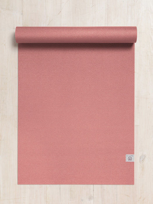 Coral textured yoga mat partially rolled up on a light wooden floor, top view, eco-friendly exercise accessory, non-slip fitness mat