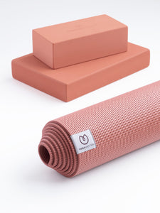Textured coral pink YOGAMATTERS yoga mat rolled up at the front and two matching yoga blocks stacked behind, shot against a white background.