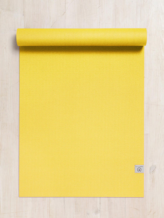Bright yellow textured yoga mat partially rolled at top, overhead view on wooden floor, non-slip surface, exercise equipment for fitness and meditation.