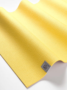 Close-up of a textured yellow yoga mat with a visible brand logo, angled side view shot on a white background.