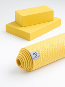 Yellow YOGAMATTERS sticky yoga mat rolled up from side view with two foam yoga blocks on white background, textured non-slip surface visible, yoga equipment, fitness accessory.