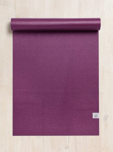 Purple yoga mat by Lululemon rolled up at one end on a wooden floor, textured non-slip surface, top view