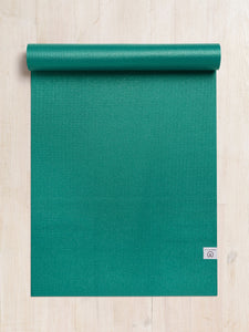 Green textured yoga mat partially rolled up on a wooden floor, top-down view, with visible brand logo on the bottom right corner.