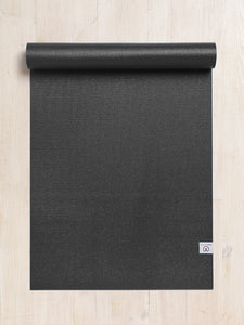 Black textured yoga mat partially rolled up on a light wooden floor, top down view, with visible brand logo in the corner.