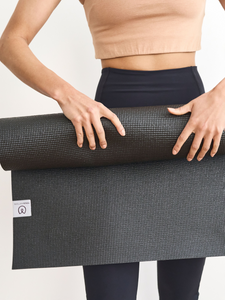 Woman rolling graphite gray textured yoga mat from front view with visible brand logo, exercise mat for yoga or fitness, non-slip surface, eco-friendly material, durable workout accessory.