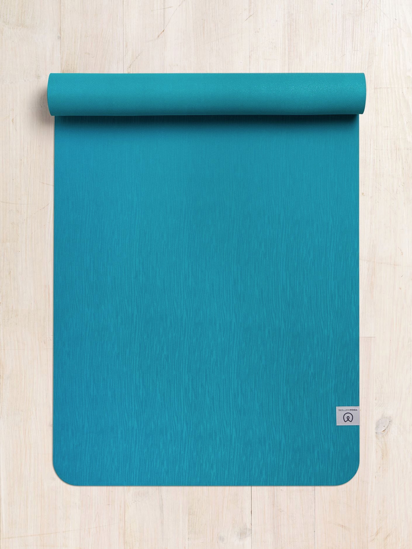 Teal yoga mat partially rolled up on a wooden floor, textured non-slip surface, top view