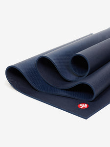 Navy blue textured yoga mat with Manduka logo, premium non-slip surface, eco-friendly material, photographed from side angle.