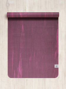 Purple textured yoga mat rolled out on a wooden floor, top view, non-slip surface, fitness and wellness equipment.