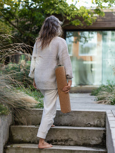 Woman in neutral-toned outfit holding cork yoga mat at outdoor home garden, side shot of durable textured non-slip exercise mat.