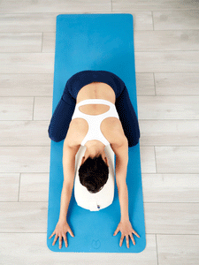 Woman practicing yoga on blue mat, top view, white and navy sports outfit, wooden floor background, non-slip texture, home fitness concept.
