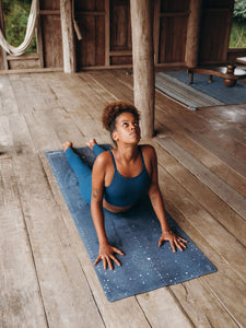 Woman practicing cobra pose on blue star-patterned yoga mat, indoor wooden floor, serene yoga studio setting