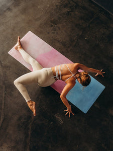 Woman practicing yoga on a gradient pink and blue yoga mat, aerial view, textured background, stylish yoga attire, dynamic yoga pose, fitness and wellness concept.