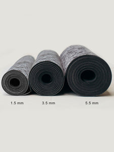 Three rolled-up yoga mats in various thicknesses displayed side by side with 1.5 mm, 3.5 mm, and 5.5 mm labels indicating thickness levels, front view on a neutral background, black color, textured surface design.