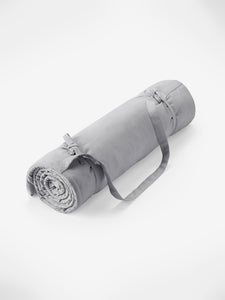 Gray rolled yoga mat with carrying strap positioned diagonally on a white background, side view, no visible brand, fitness and wellness equipment.