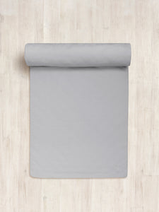 Gray yoga mat partly rolled up on a wooden floor with visible brand logo on the bottom right corner, top view shot.
