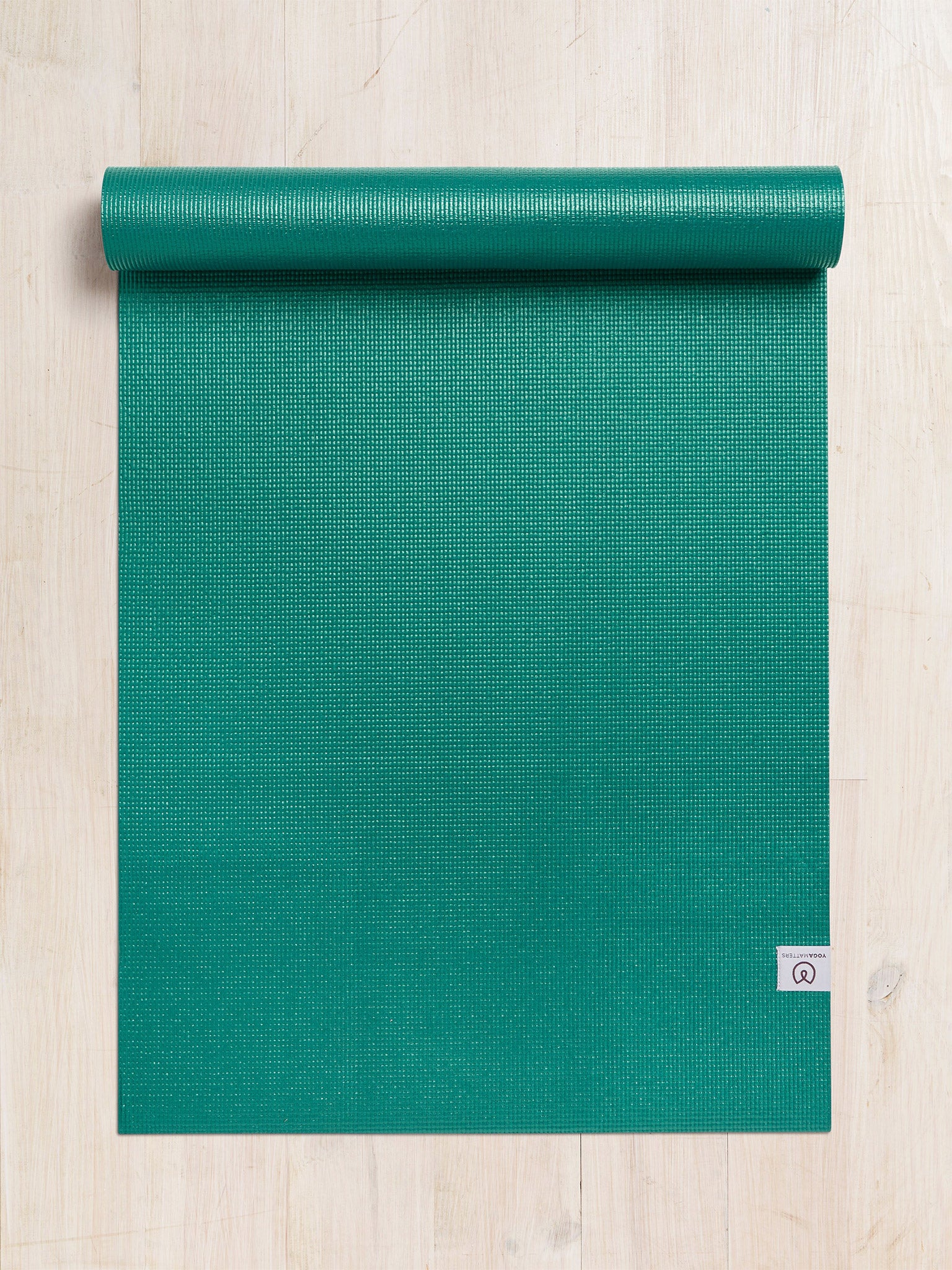 Green yoga mat partially rolled with visible brand logo on textured wooden floor, top view.