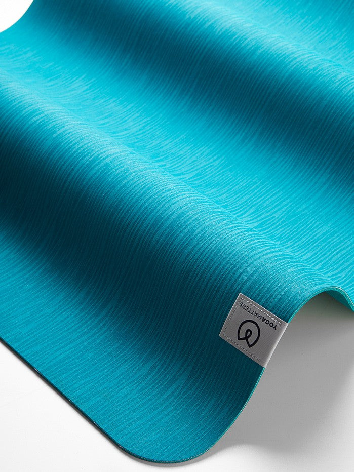 Teal textured yoga mat by Lululemon, close-up side view showing brand logo, non-slip exercise mat for fitness and meditation.