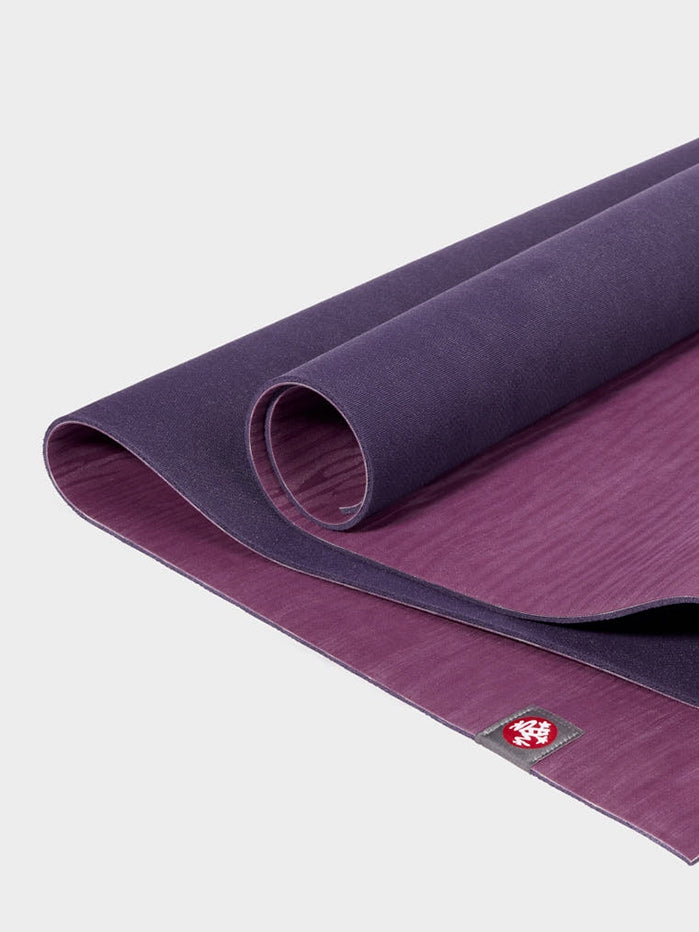 Purple yoga mat rolled halfway, high quality, non-slip surface, branded with a red mandala logo, close-up, product shot.
