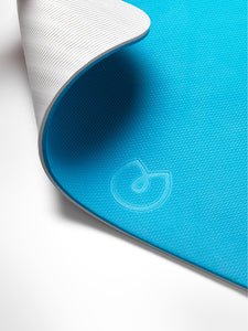 Blue textured yoga mat with rolled edge and white underside, close-up side view showing grippy surface and embossed logo.