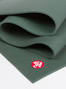 Dark green textured yoga mat partially unrolled with visible red logo, photographed from an angled side view, highlighting the mat's non-slip surface and thickness.