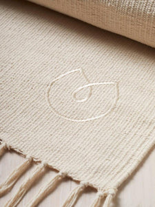 Beige yoga mat with tassels and embossed logo, eco-friendly natural rubber non-slip surface, close-up side shot.