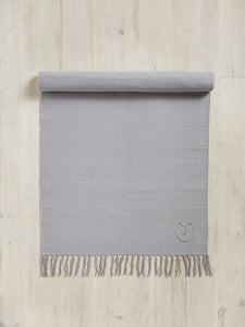Gray textured yoga mat with fringe rolled half way on wooden floor, top view, with visible brand logo.