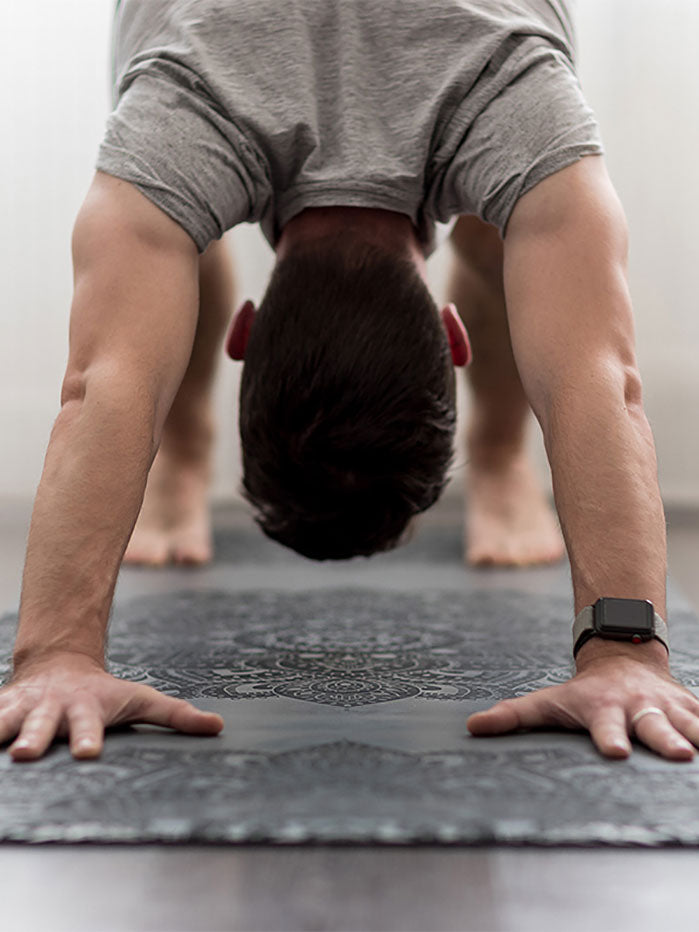 Man practicing yoga on a textured gray yoga mat with intricate pattern, shot from the front in a well-lit room.